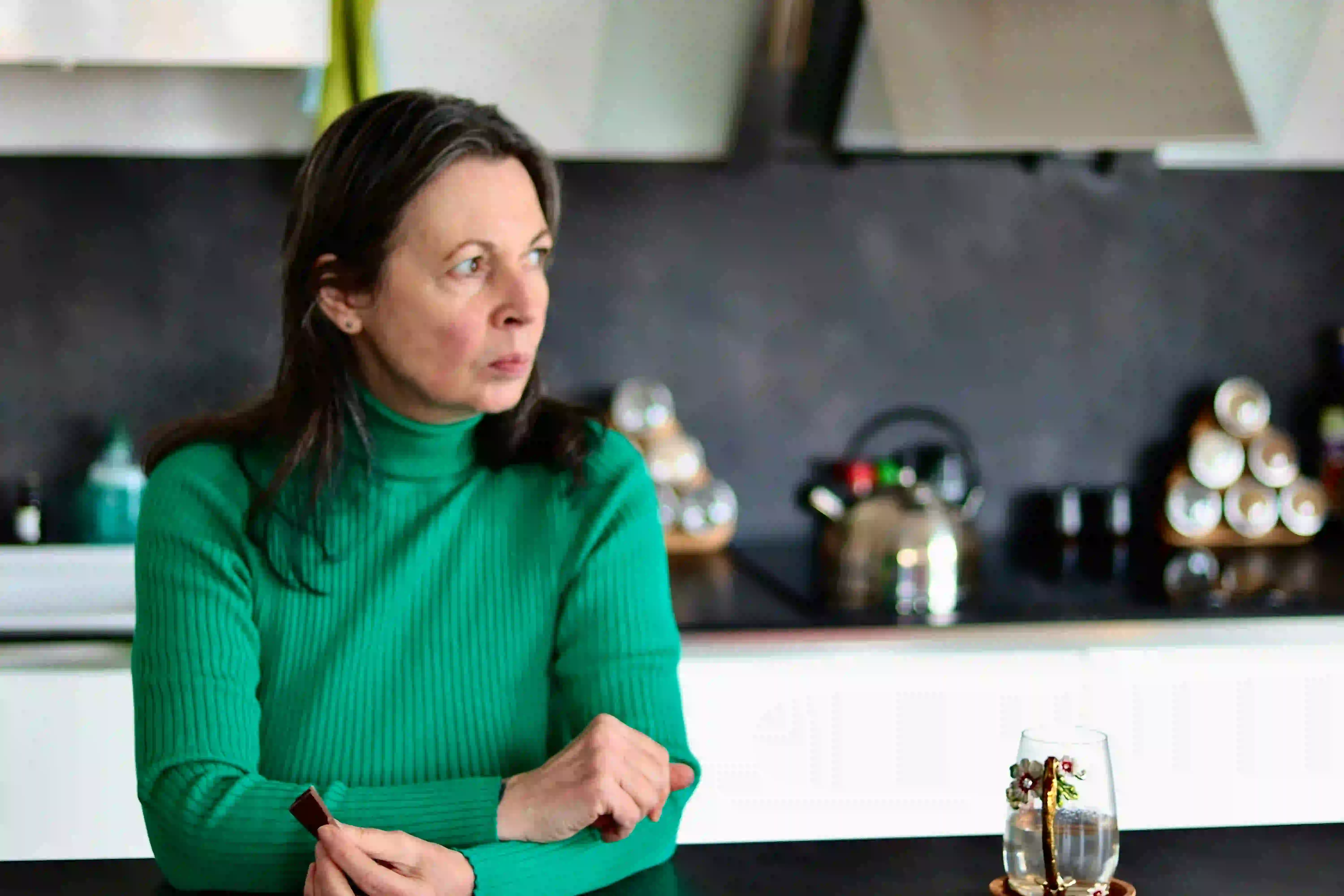 A woman in her fifties sitting at her kitchen table, looking away thoughtfully